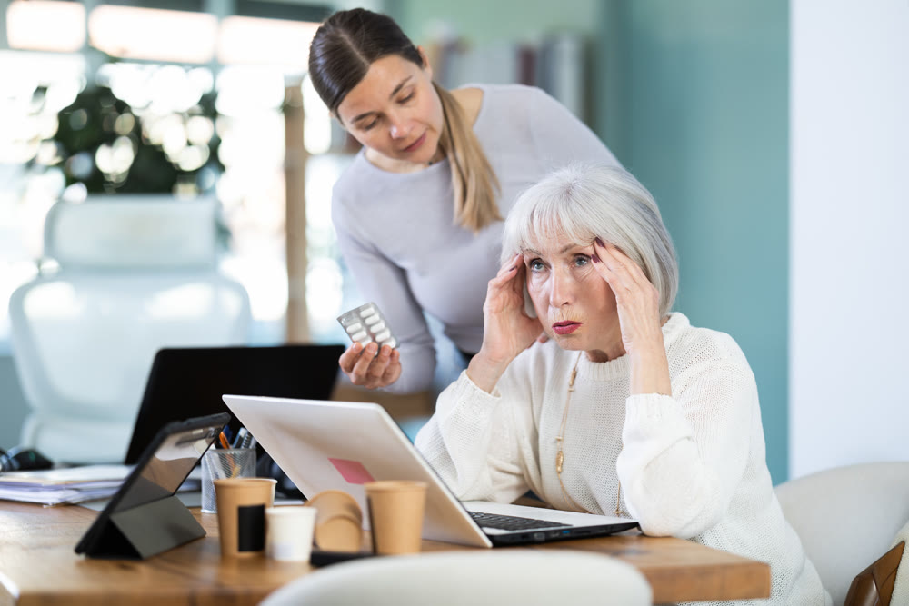 Adult woman sympathizes to sick senior female manager with headache and offers pain pills.