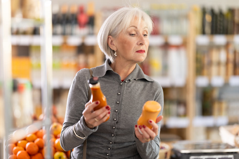 Choose food in supermarket - woman chooses sauce or ketchup to buy in the grocery department section of store