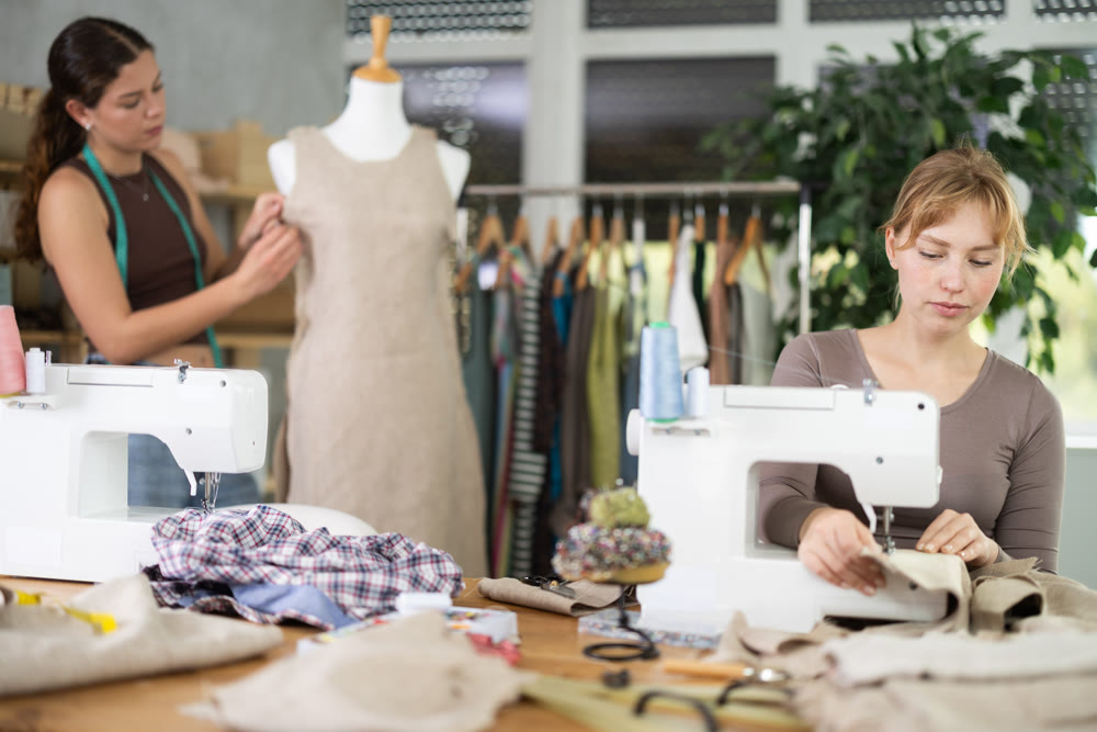 Young tailoress using sewing-machine while other working with mannequin