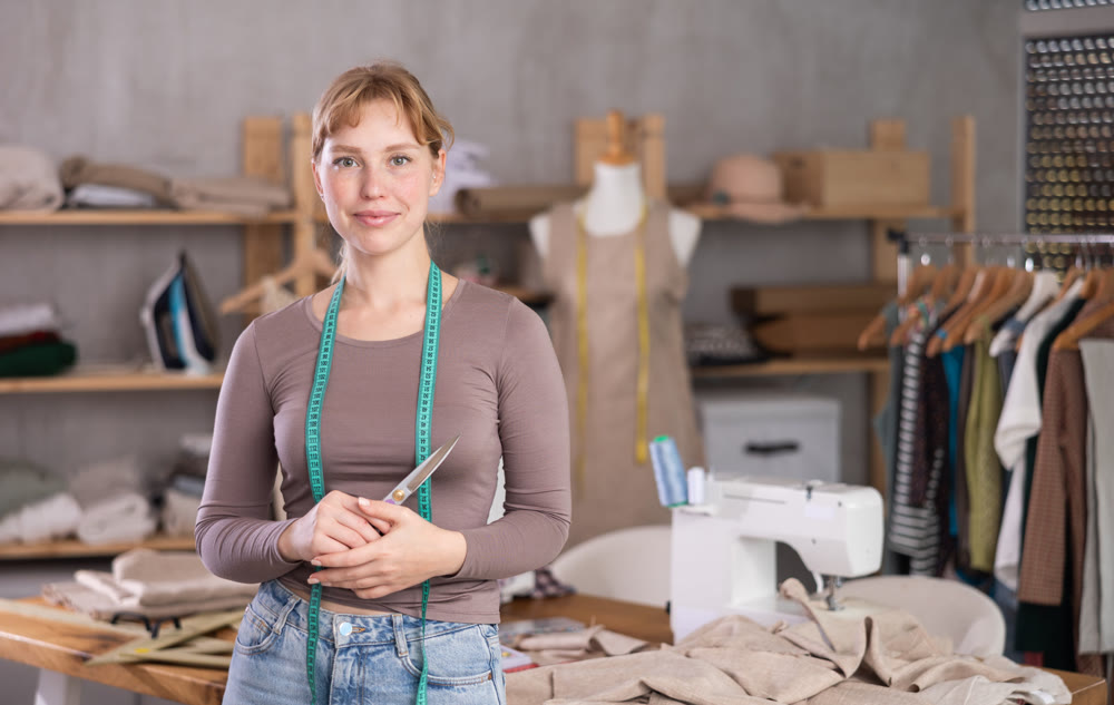 Smiling young female dressmaker posing in sewing studio