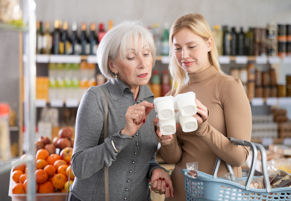 Girl and grandmother buyers examine good, doubt and choose yogurt in store