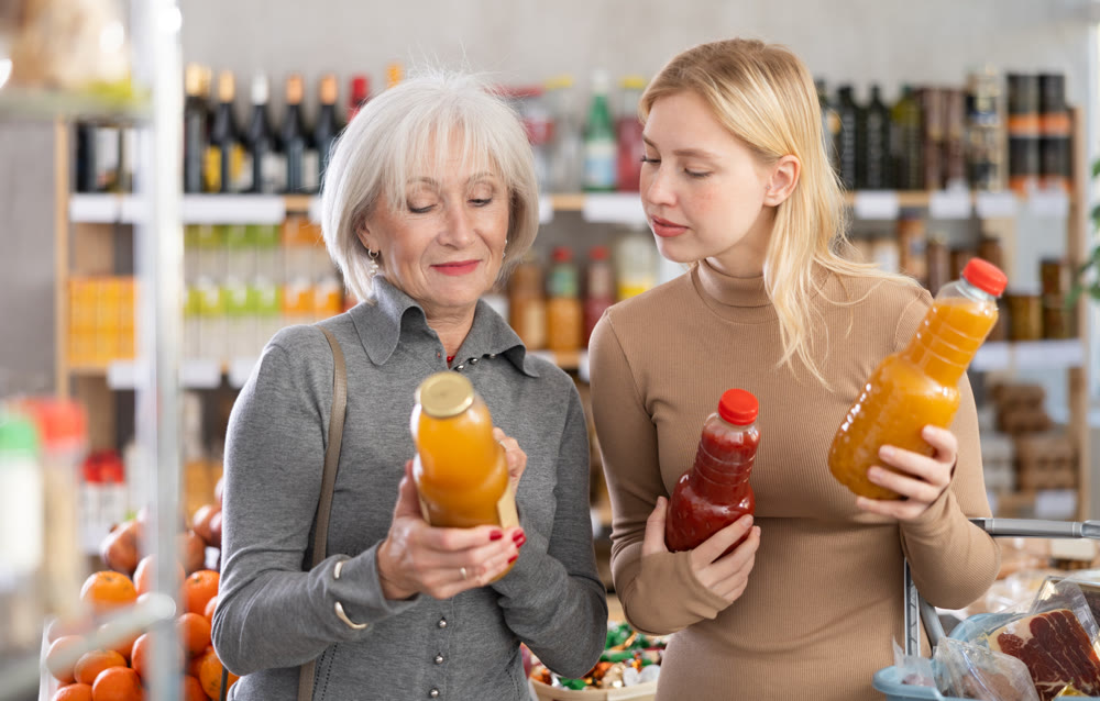 Girl and grandmother buyers examine good, doubt and choose between varieties of fruit juice in store