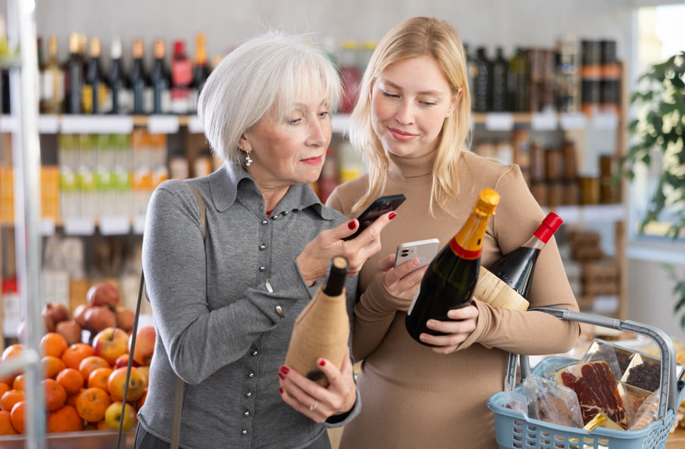 Elderly mother and her adult daughter scan a QR code on a bottle of wine label together to check expiration date