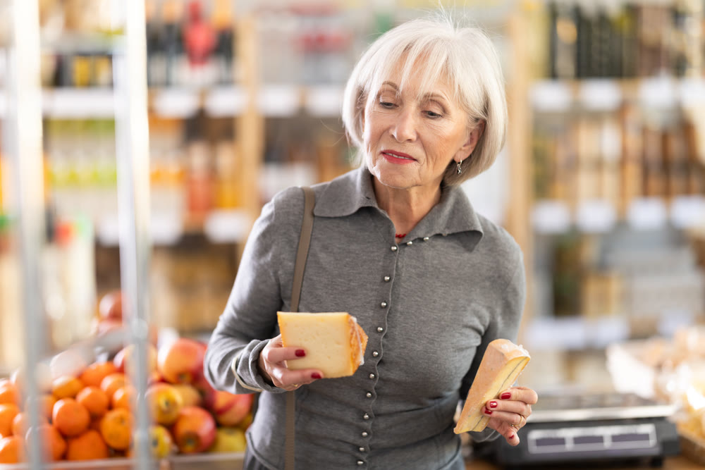 Elderly woman choosing cheese in grocery store