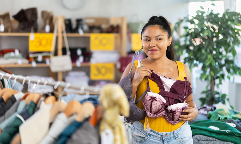 Happy young girl choosing bra in clothing store