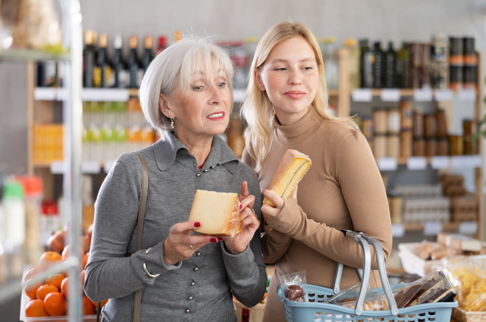 Girl and grandmother buyers examine good, doubt and choose cheese in store