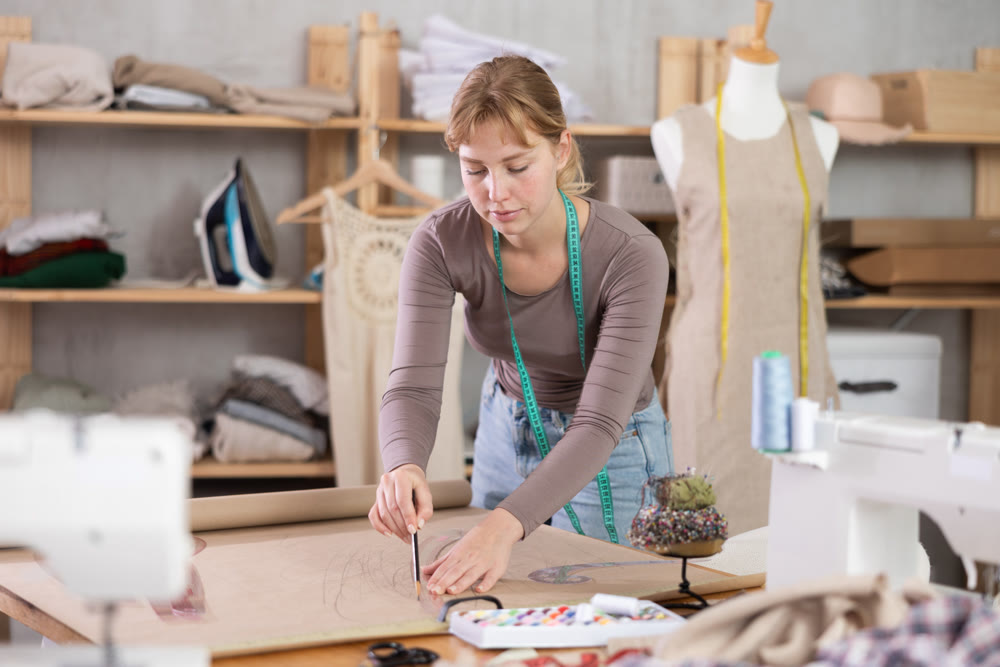 Female seamstress drawing sewing pattern on paper in studio