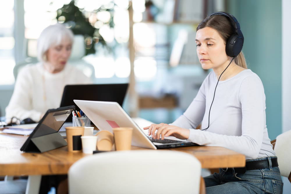Two businesswomen work on laptops in modern company office