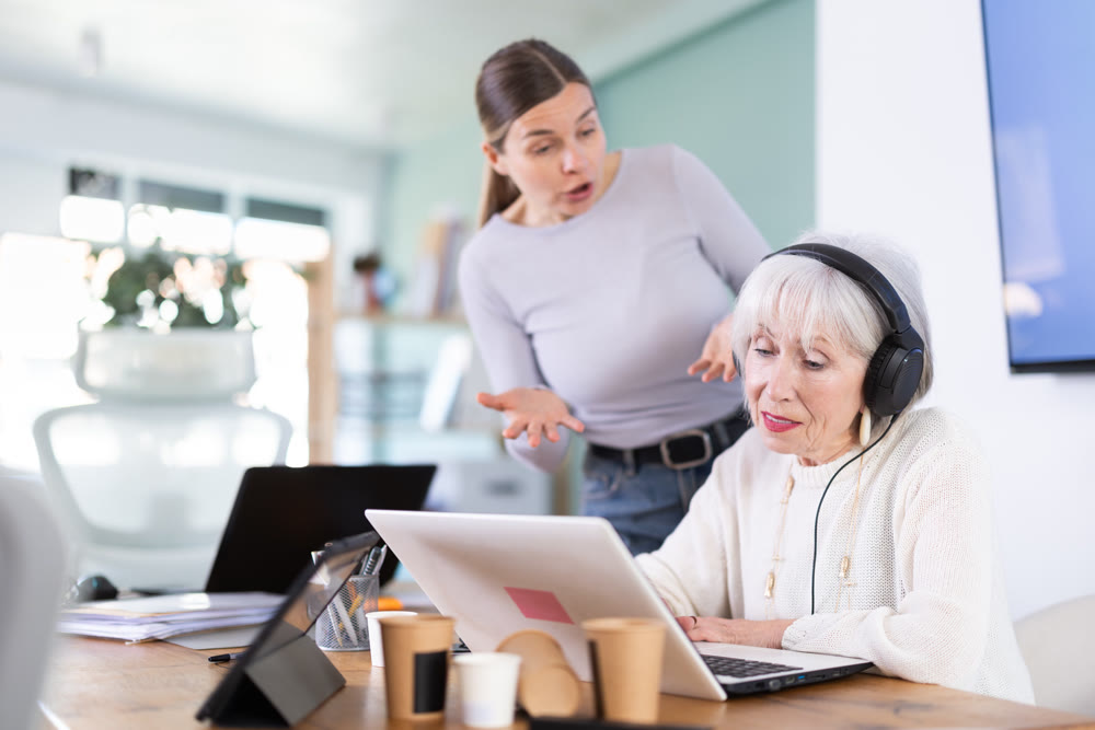 Adult woman scolding female colleague with headphones at laptop