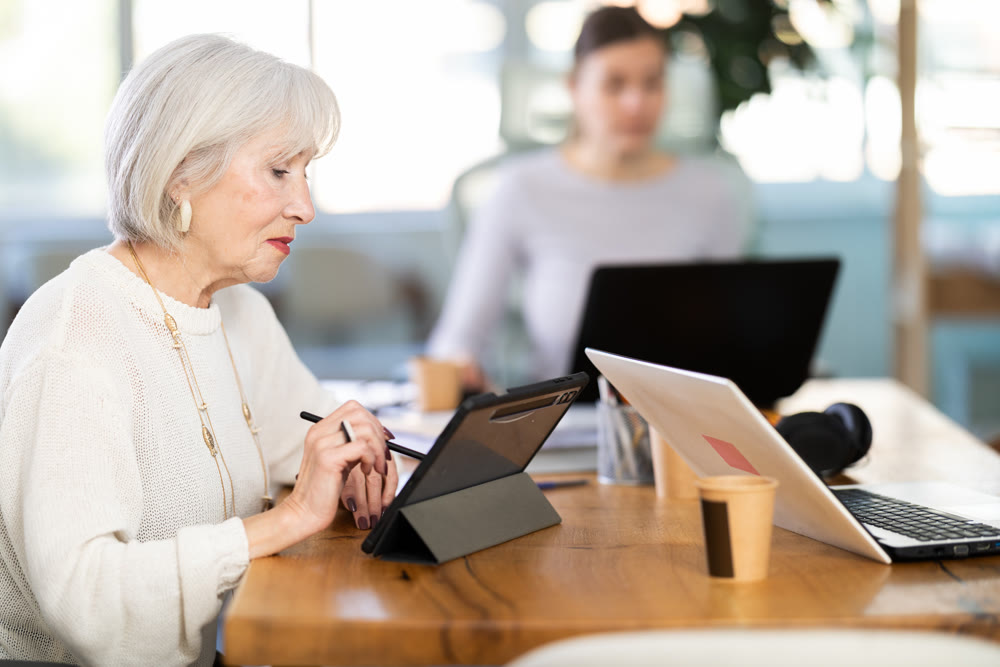 Two businesswomen work on laptops in modern company office