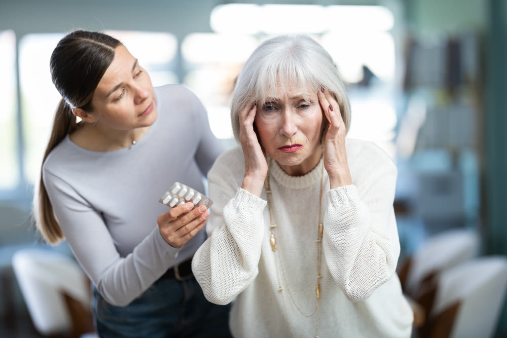 Adult woman sympathizes to sick senior female manager with headache and offers pain pills.