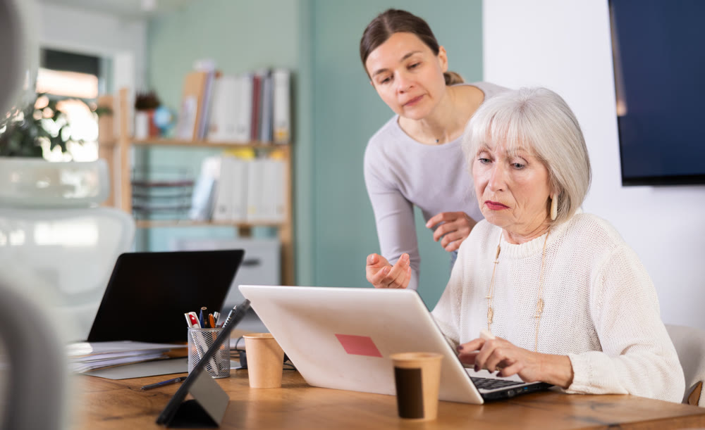 Female boss help to mature female interns with laptop task