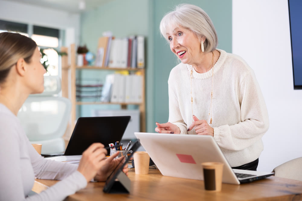 Two businesswomen work on laptops in modern company office