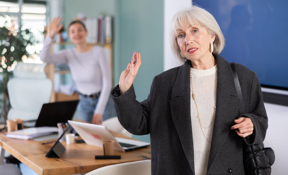 Elderly woman leaving office saying goodbye to colleague