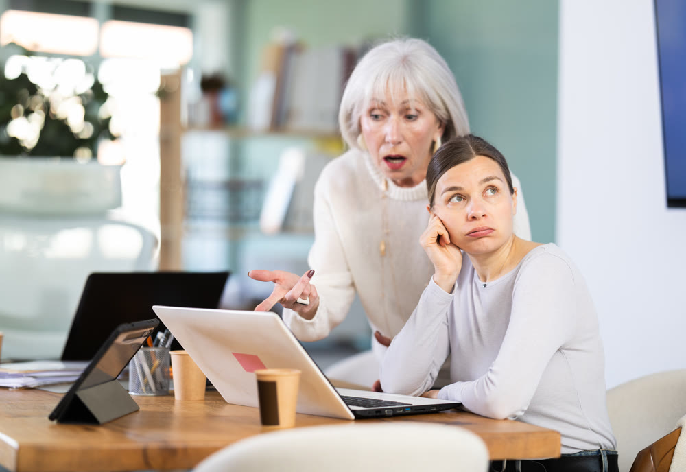 Female mature boss yells at woman employee, staff work at computer