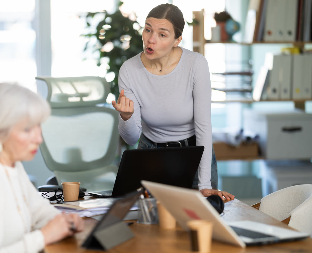 Female boss yells at senior woman employee, pensioner work at tablet