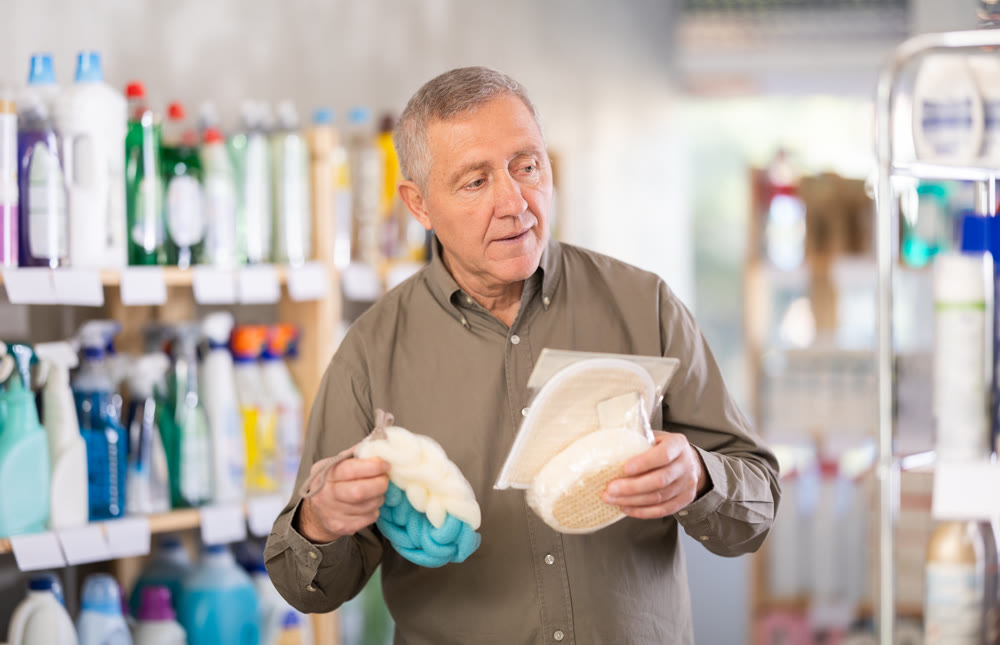 Elderly man buys shampoo, body wash and loofah in the household goods section of supermarket
