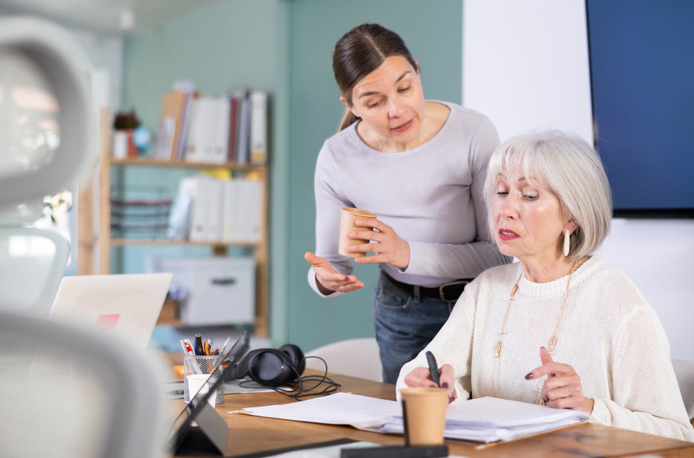 Boss help an older employee learn to use laptop