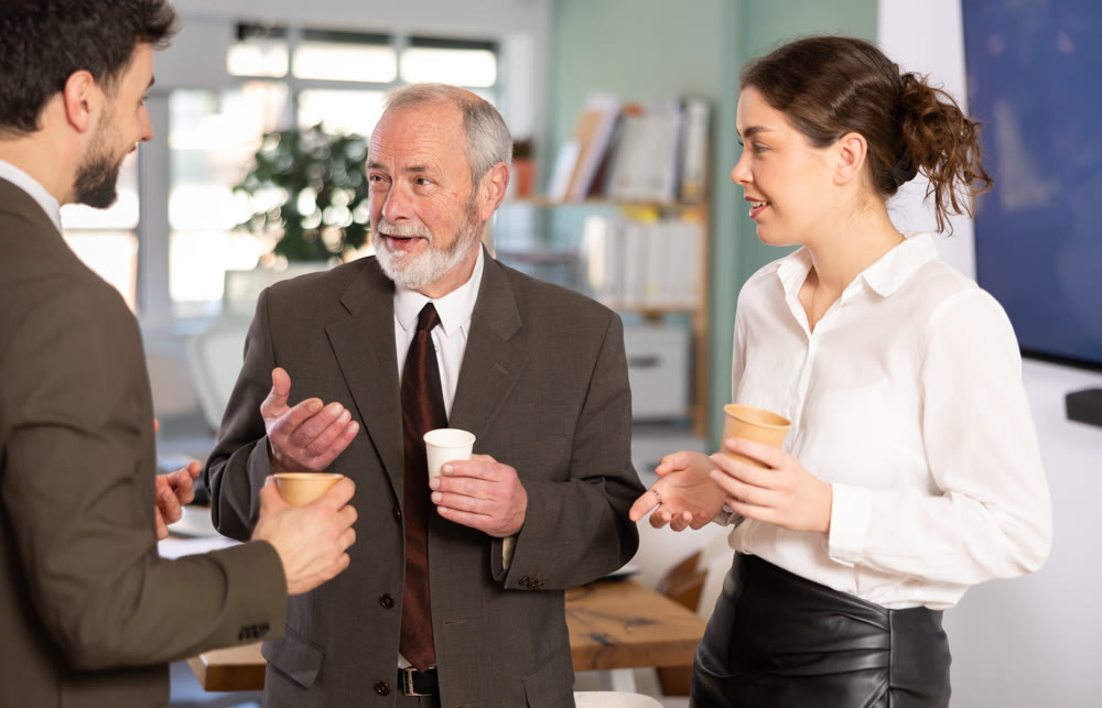Coffee break - men and young woman drink coffee and chat lively with each other in modern office