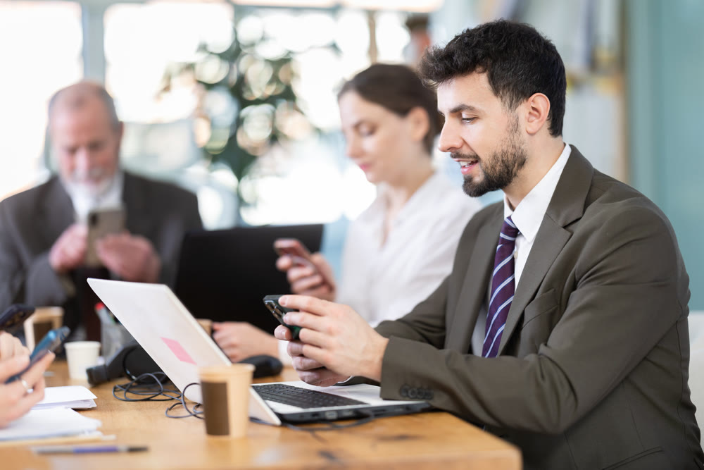 Concentrated man office worker scrolling smartphone sitting at workplace in office of business company
