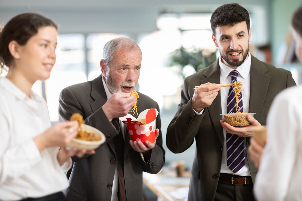 Group of colleagues, man and woman, are having lunch in office during their break, eating noodles