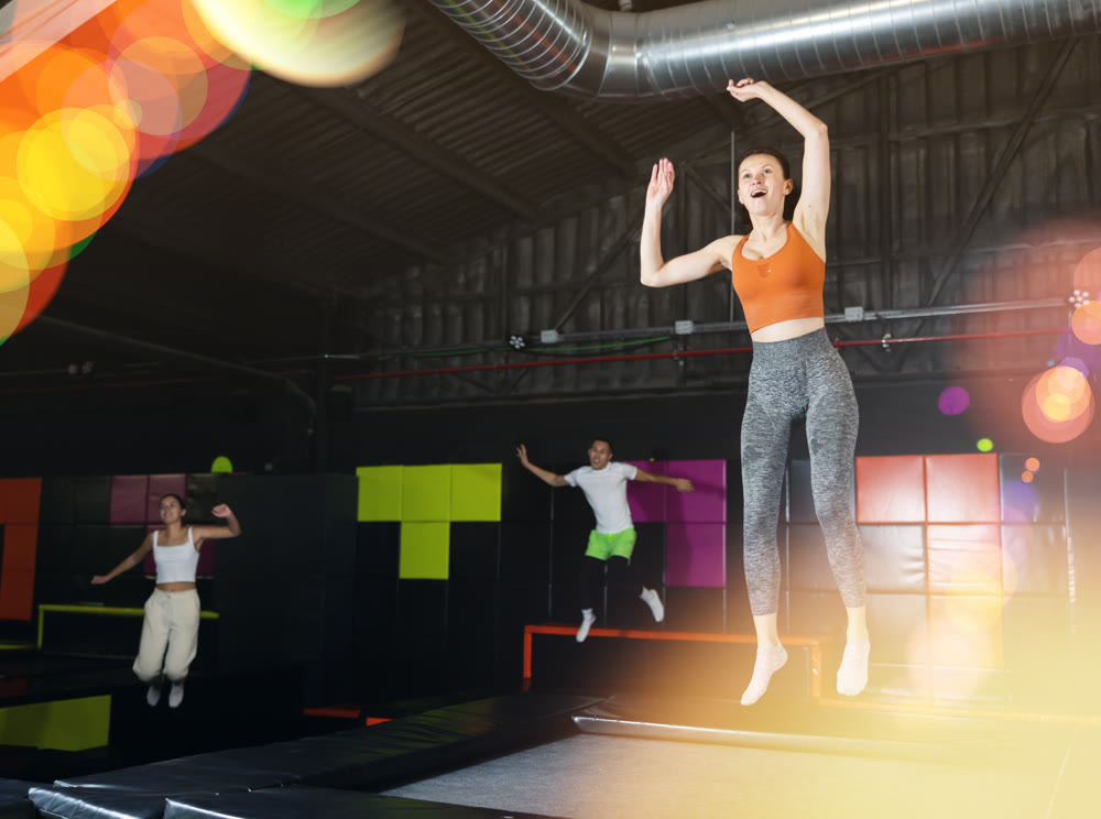 Happy middle aged woman practicing and jumping on trampolines in a sports indoor center, workout and modern entertainment concept