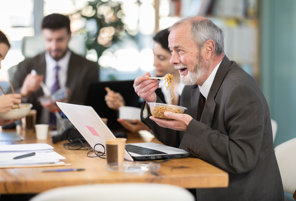 Lunch break - mature man eating noodles with colleagues in modern office