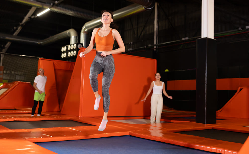 Enthusiastic woman leaping at vibrant trampoline gym with friends