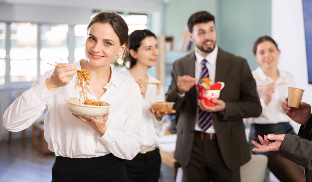 Lunch break - woman eating noodles with colleagues in modern office
