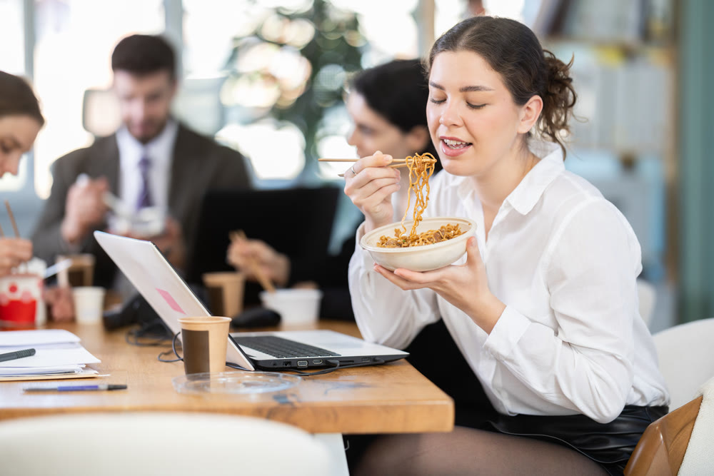 Lunch break - woman eating noodles with colleagues in modern office