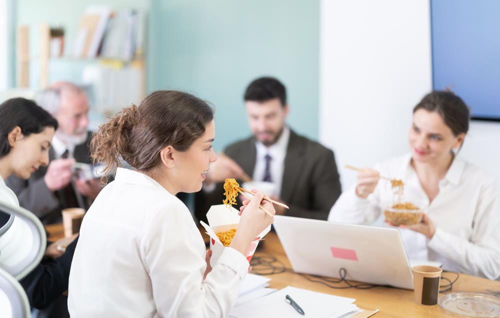 Group of colleagues, man and woman, are having lunch in office during their break, eating noodles