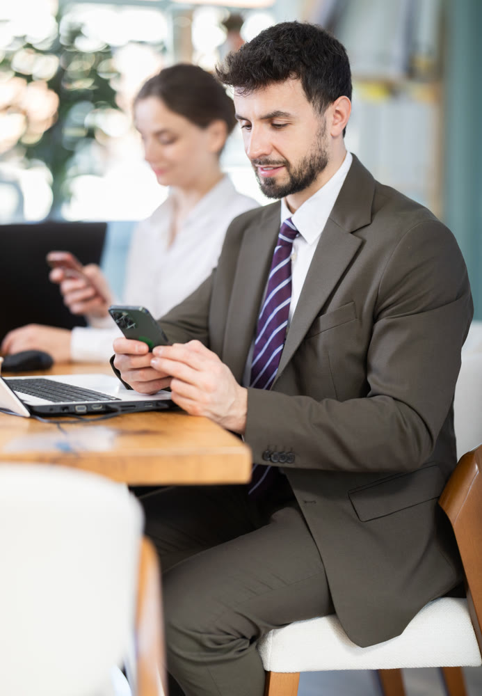 Man scrolls feed and passes time on social media. Bored staff on smartphone in background