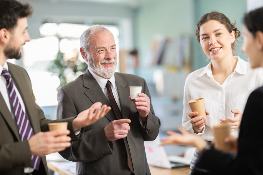 Friendly co-workers employees drinking hot coffee and talking during break while working in office