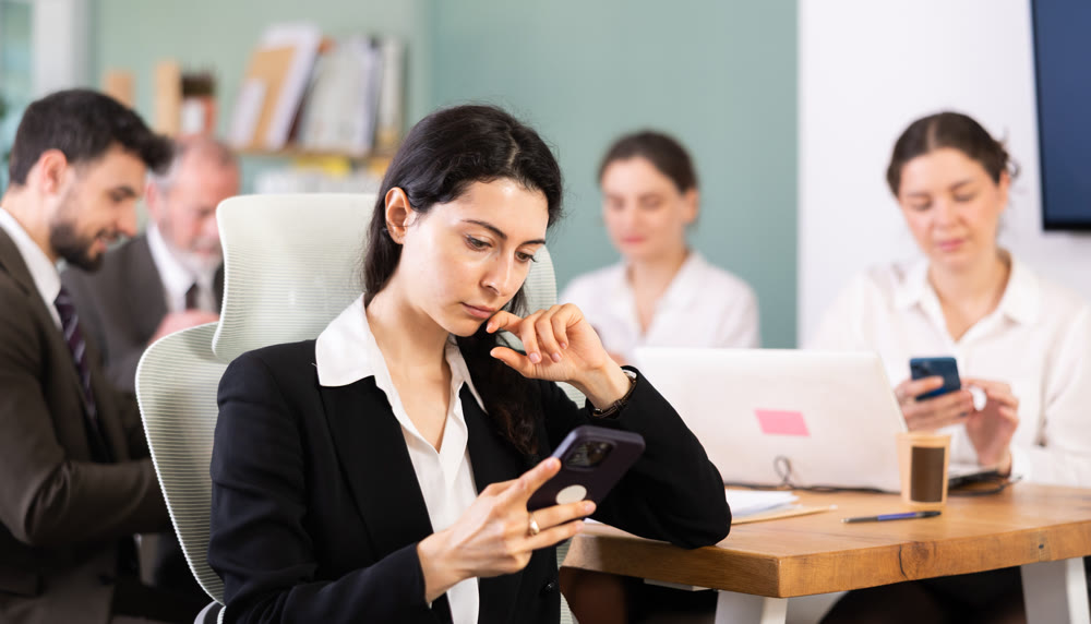 Girl scrolls feed and passes time on social media. Bored staff on smartphone in background