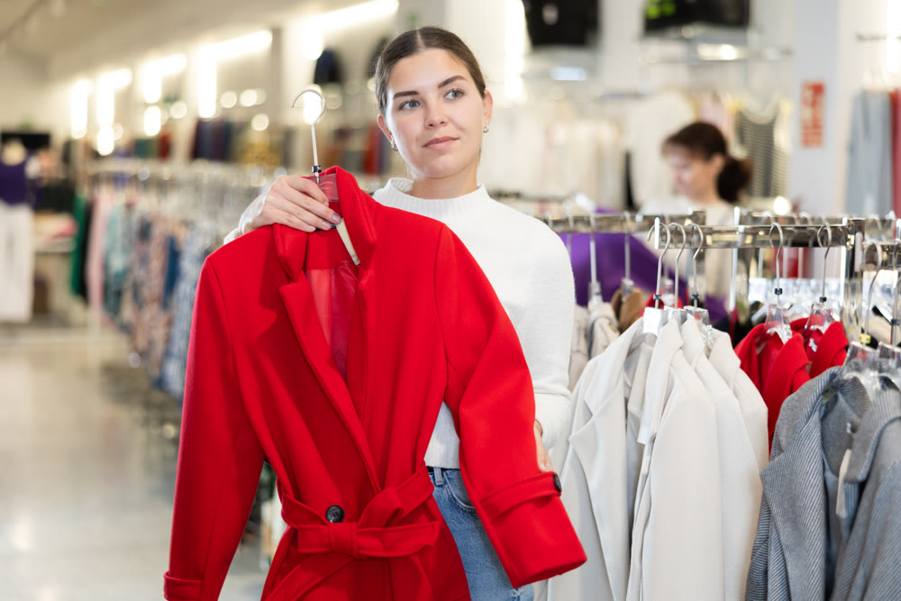 Young girl choosing unicolorous coat in clothing shop
