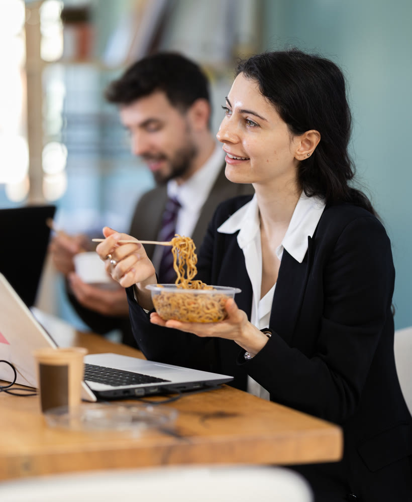 Lunch break - woman eating noodles with colleagues in modern office