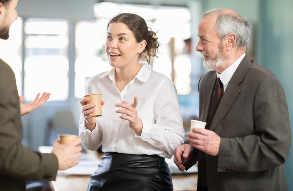 Coffee break - men and young woman drink coffee and chat lively with each other in modern office