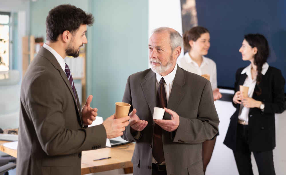 Two man co-workers employees drinking hot coffee and talking during break while working in office