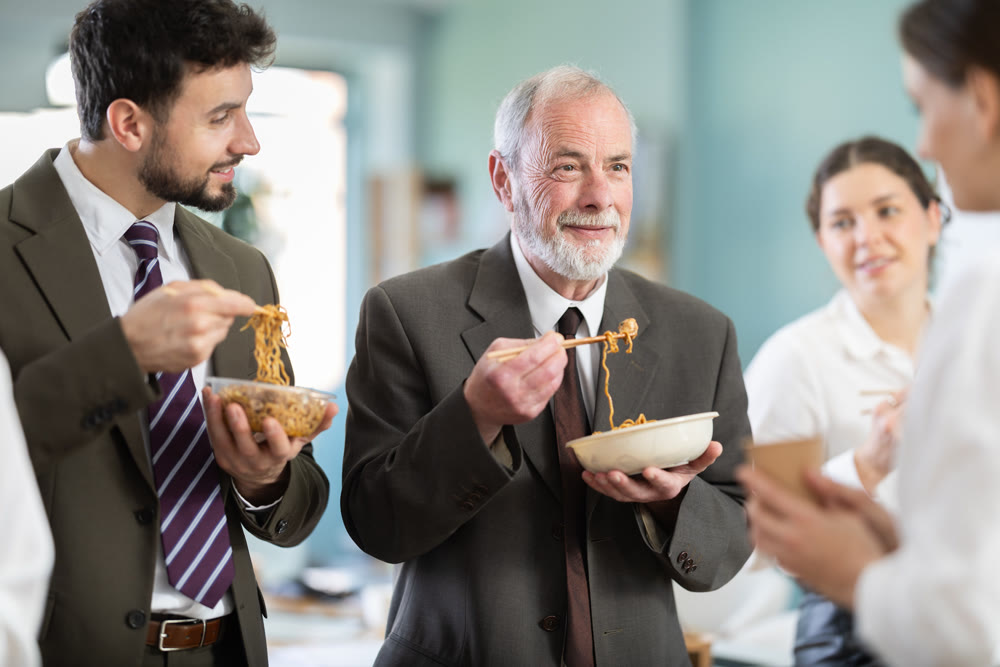 Group of colleagues, man and woman, are having lunch in office during their break, eating noodles