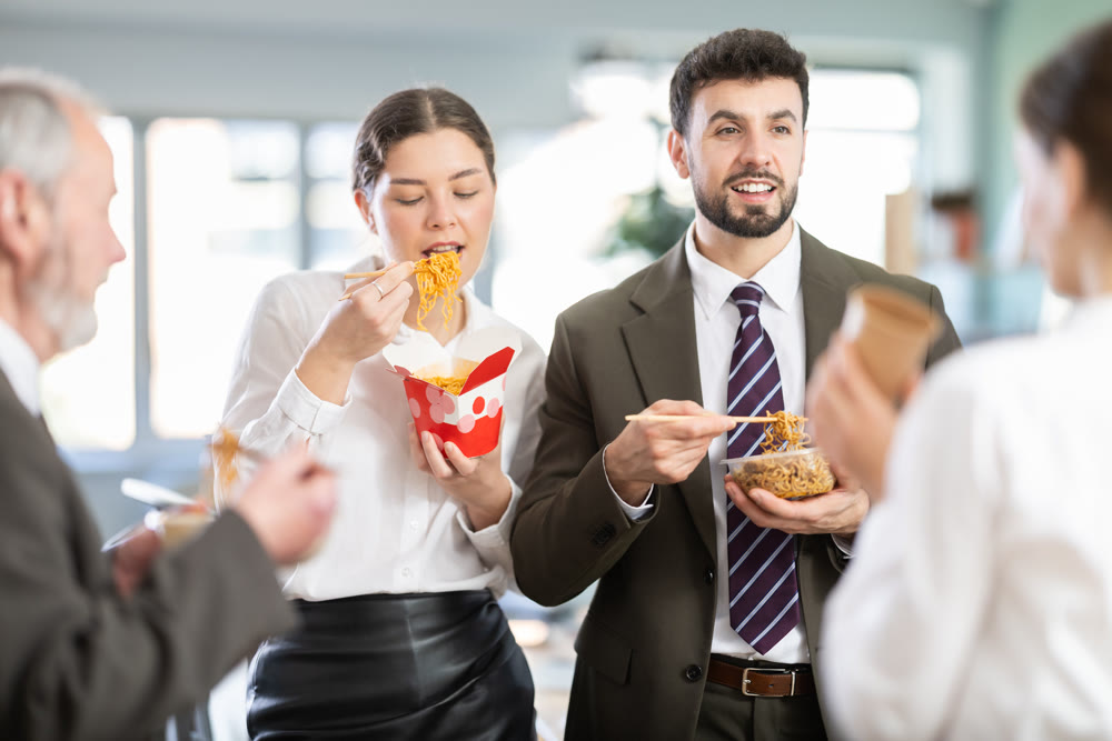 Group of friendly young office workers different ages standing and eating fast food at modern office canteen