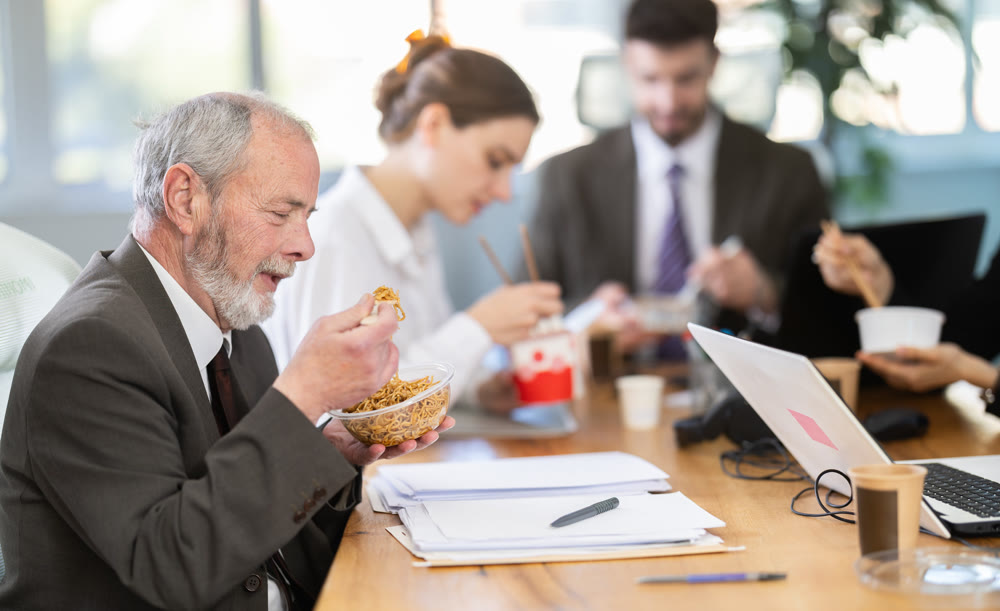 Lunch break - mature man eating noodles with colleagues in modern office
