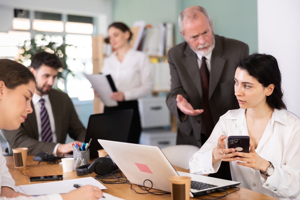 Senior manager scolds young female employee for talking on mobile phone while working in office