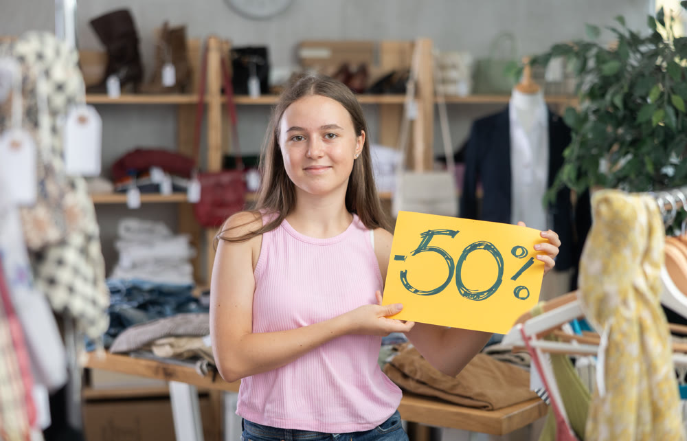 Teen girl holding sign saying 50 percent discount in clothing store