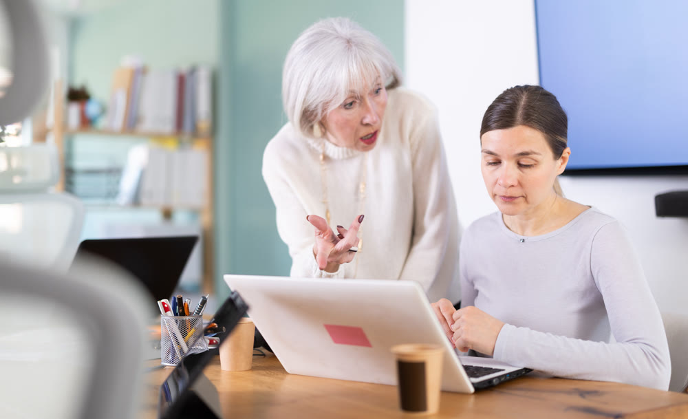 Elderly woman scolding adult female colleague working on laptop