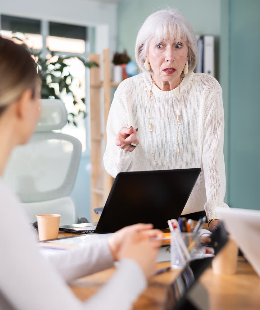 Elderly woman scolding female colleague working on tablet