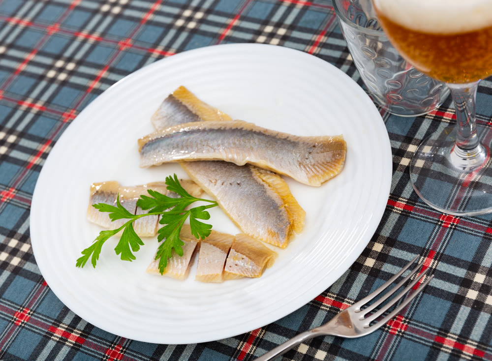 On table is plate with appetizer - salted Atlantic herring fillet decorated with parsley