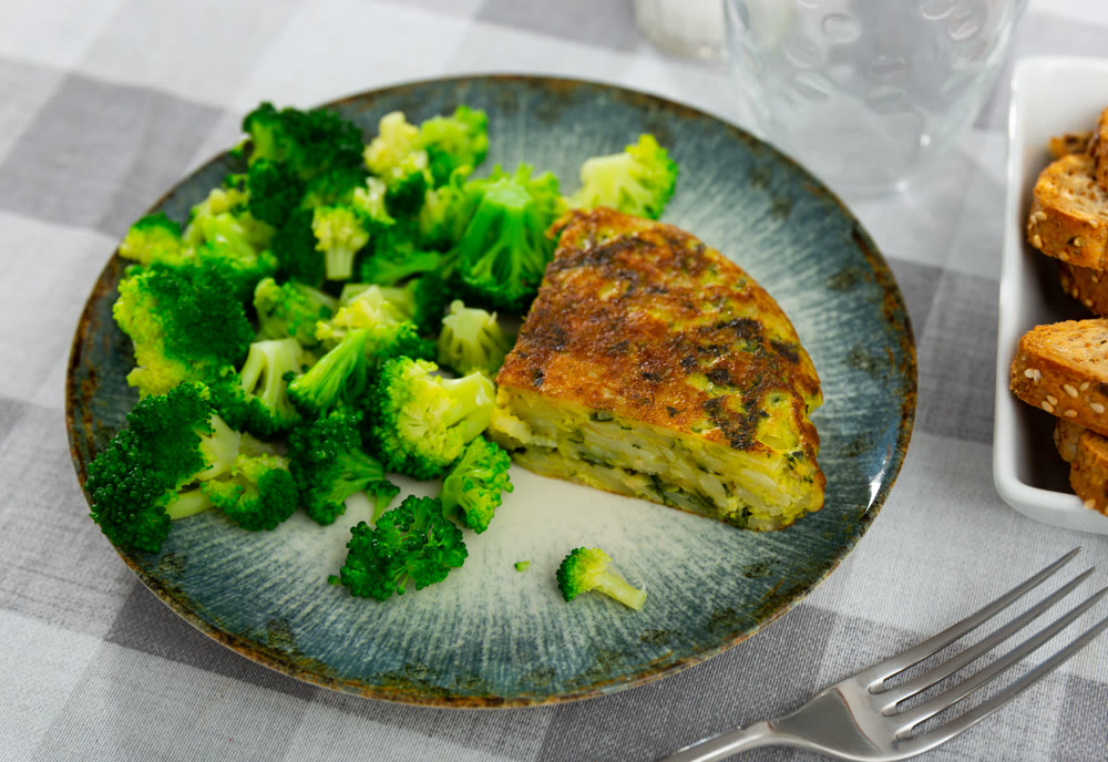On plate is triangular piece of omelet with asparagus flecks, garnished with broccoli cabbage.