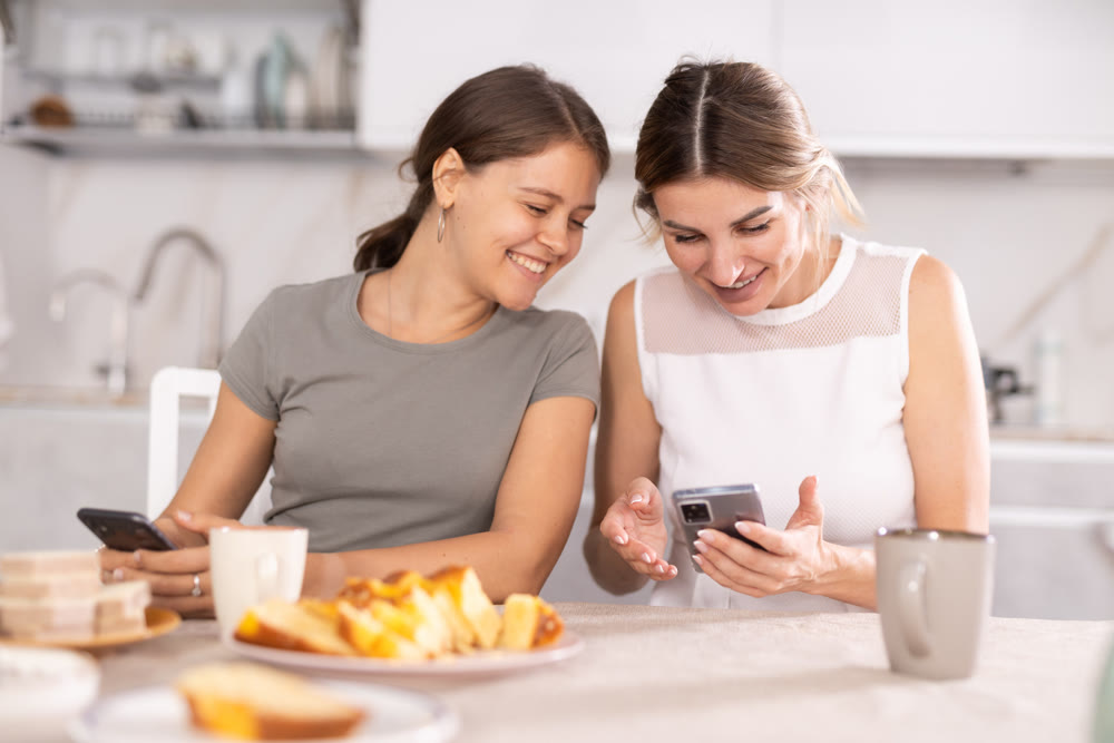 Two girls in kitchen are discussing what they saw on their smartphone