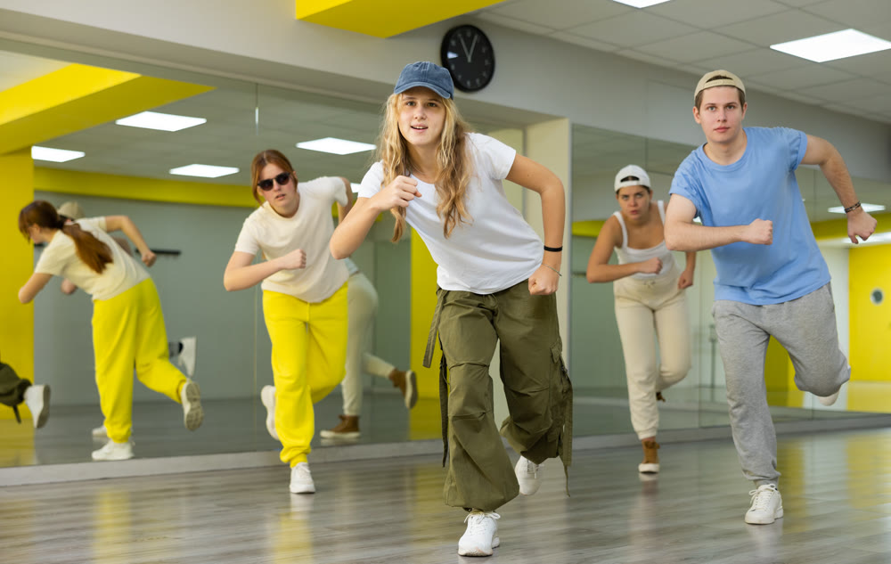 Group of teenagers in casual clothes training hip hop in class, posing and having fun