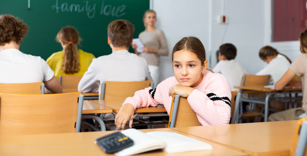 Sad young schoolgirl sitting at desk during lesson
